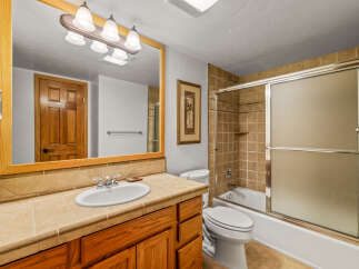 This bathroom features a spacious vanity with a tiled countertop and wooden cabinetry, complemented by a large mirror with an ornate light fixture.