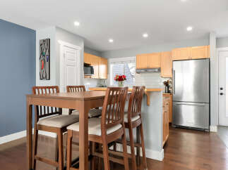 This modern kitchen and dining area features a sleek stainless steel refrigerator and light wood cabinetry, complemented by a stylish high-top dining table with comfortable seating.