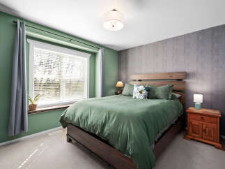 This inviting bedroom features a comfortable queen-size bed dressed in serene green linens, complemented by a textured gray accent wall.