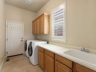 This spacious laundry room features a convenient side-by-side washer and dryer setup, complemented by ample storage with overhead cabinets and a base cabinet with a large sink.