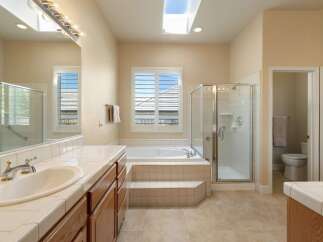 This spacious bathroom features a luxurious soaking tub with tiled steps, a separate glass-enclosed shower, and a dual vanity with ample counter space.