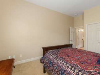 This bedroom features a comfortable queen-size bed with a striking red and blue patterned comforter, set against a neutral beige wall.