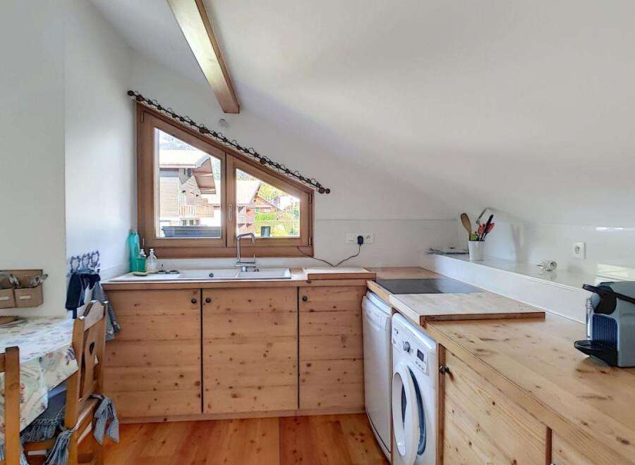 Discover this charming attic kitchen featuring warm wooden cabinetry and countertops, complemented by a unique triangular window offering scenic views.