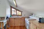 Discover this charming attic kitchen featuring warm wooden cabinetry and countertops, complemented by a unique triangular window offering scenic views.