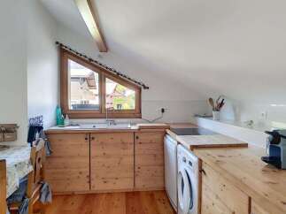 Discover this charming attic kitchen featuring warm wooden cabinetry and countertops, complemented by a unique triangular window offering scenic views.