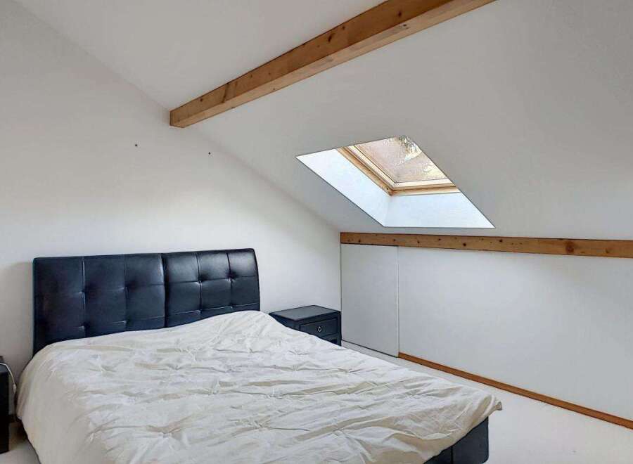 Discover this charming attic bedroom featuring a comfortable bed with a stylish black headboard and a cozy duvet.