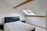 Discover this charming attic bedroom featuring a comfortable bed with a stylish black headboard and a cozy duvet.