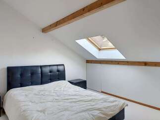 Discover this charming attic bedroom featuring a comfortable bed with a stylish black headboard and a cozy duvet.