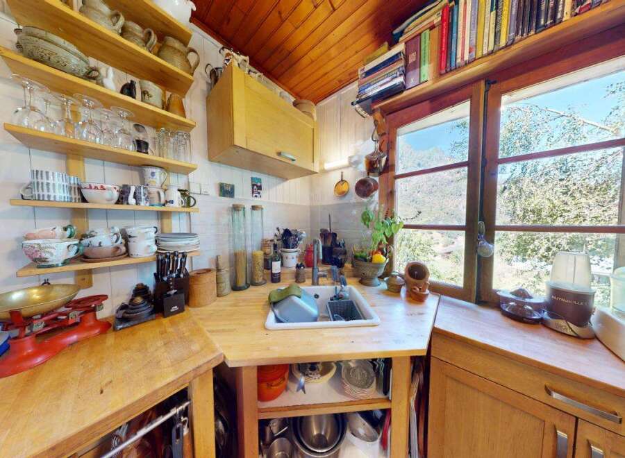 Charming rustic kitchen featuring open shelving stocked with glassware and pottery, a vintage red scale, and a large farmhouse sink.