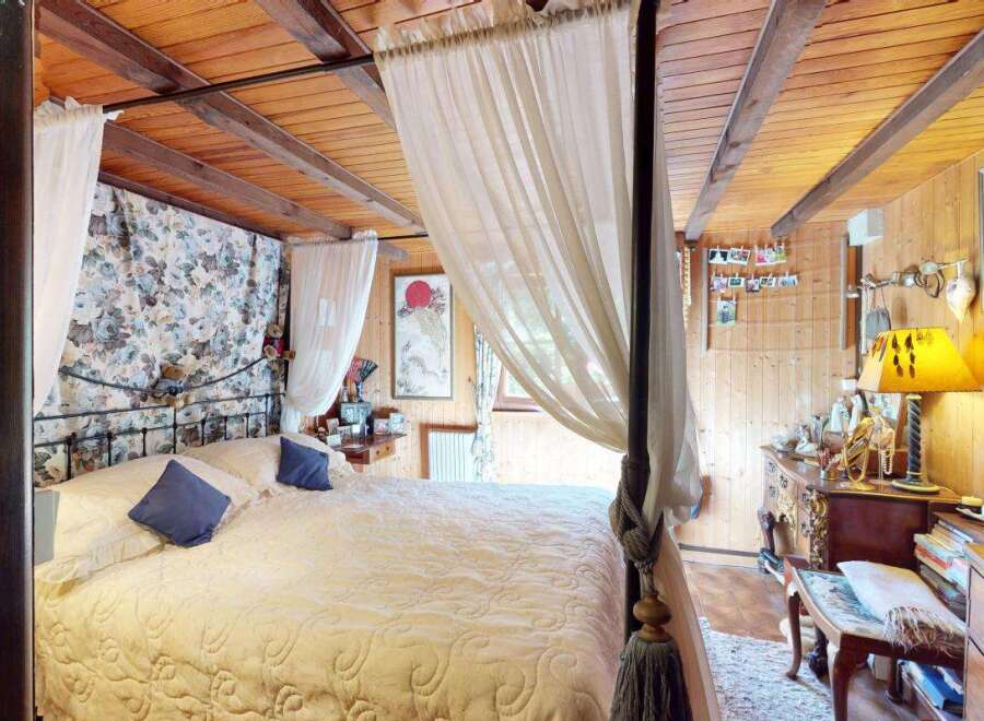 Experience rustic charm in this cozy bedroom featuring a beautiful four-poster bed draped with sheer curtains.