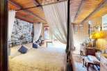Experience rustic charm in this cozy bedroom featuring a beautiful four-poster bed draped with sheer curtains.