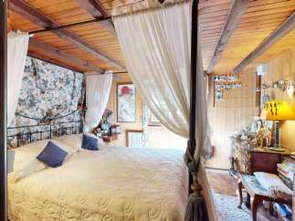 Experience rustic charm in this cozy bedroom featuring a beautiful four-poster bed draped with sheer curtains.