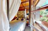 Experience serene living in this charming bedroom, featuring a comfortable bed draped with elegant white curtains and a floral patterned headboard.