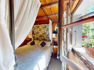 Experience serene living in this charming bedroom, featuring a comfortable bed draped with elegant white curtains and a floral patterned headboard.