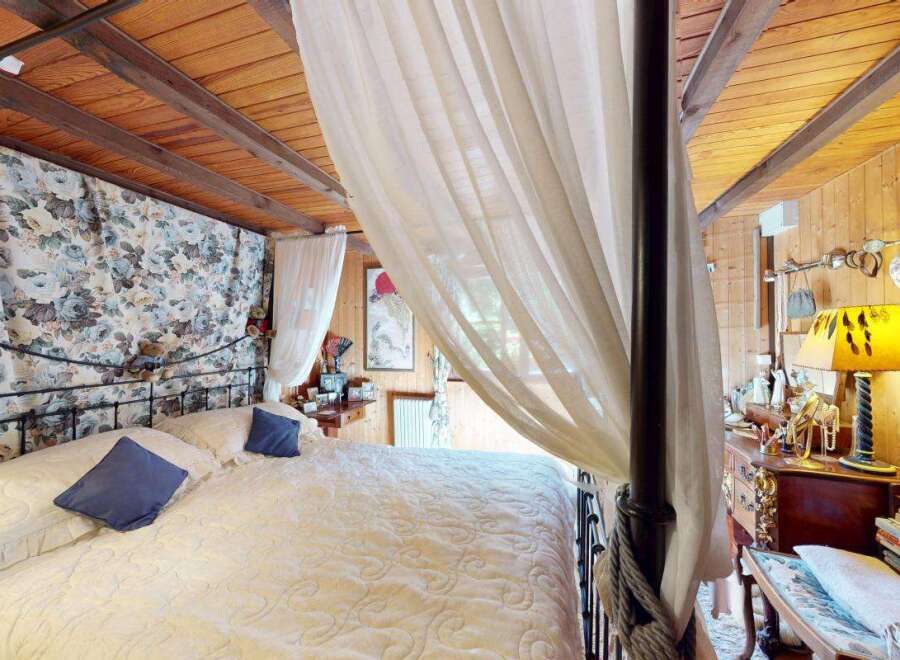 Experience rustic charm in this cozy bedroom featuring a beautiful four-poster bed adorned with floral drapes and sheer white curtains.