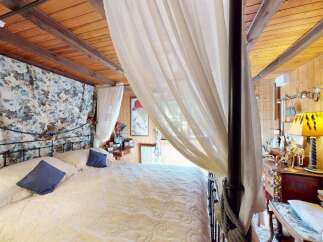 Experience rustic charm in this cozy bedroom featuring a beautiful four-poster bed adorned with floral drapes and sheer white curtains.