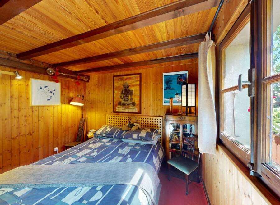 Experience cozy living in this charming wood-paneled bedroom, featuring a comfortable bed with a patterned duvet and a unique wooden headboard.