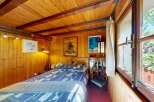 Experience cozy living in this charming wood-paneled bedroom, featuring a comfortable bed with a patterned duvet and a unique wooden headboard.