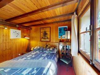 Experience cozy living in this charming wood-paneled bedroom, featuring a comfortable bed with a patterned duvet and a unique wooden headboard.