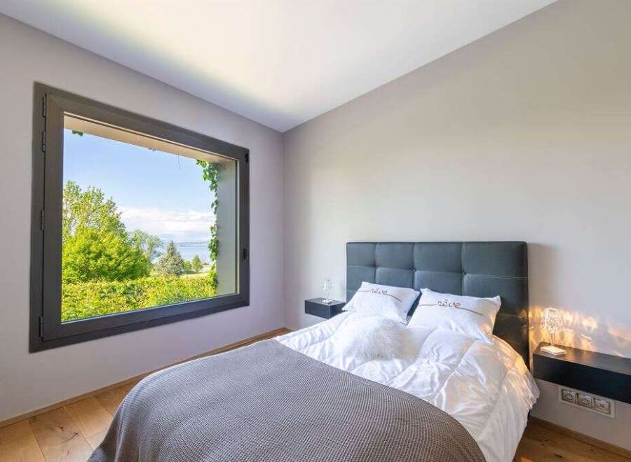Experience serene living in this beautifully appointed bedroom, featuring a large window that frames a breathtaking view of lush greenery and a tranquil body of water.