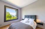 Experience serene living in this beautifully appointed bedroom, featuring a large window that frames a breathtaking view of lush greenery and a tranquil body of water.