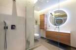 Experience modern luxury in this stunning bathroom featuring a sleek walk-in shower with a rainfall showerhead and a contemporary vanity with a backlit circular mirror.
