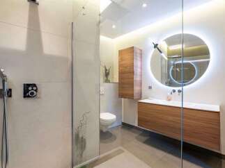Experience modern luxury in this stunning bathroom featuring a sleek walk-in shower with a rainfall showerhead and a contemporary vanity with a backlit circular mirror.