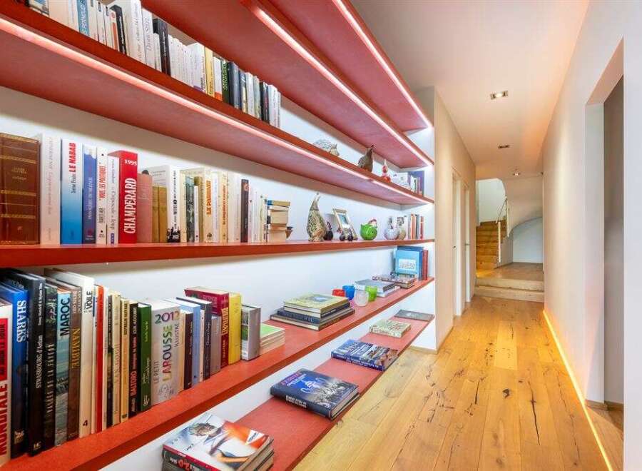 This hallway features a striking modern design with vibrant red shelving units illuminated by subtle LED lighting, creating a warm and inviting ambiance.