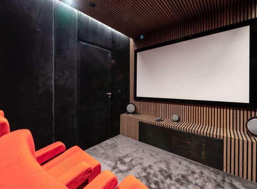 Experience cinematic bliss in this state-of-the-art home theater, featuring plush orange seating and a massive projection screen for an immersive viewing experience.