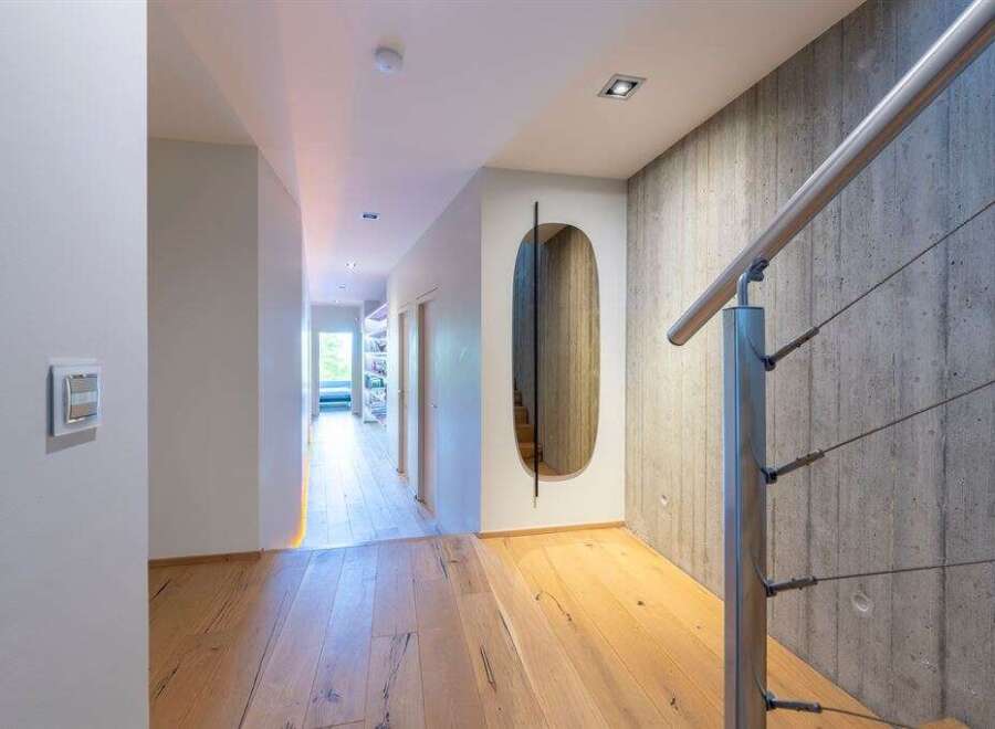 Experience modern living in this stunning hallway featuring a sleek metal handrail against a textured concrete wall.