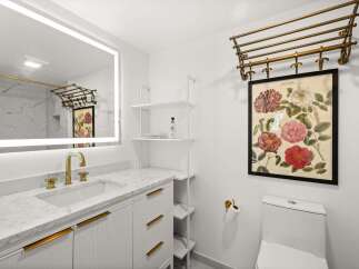 This modern bathroom features a sleek vanity with a marble countertop and gold accents, complemented by a large illuminated mirror.