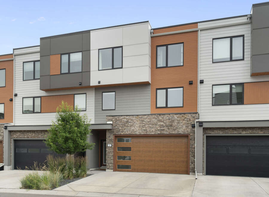 Discover modern living in this stunning townhouse featuring a striking facade with a mix of wood-grain siding, stone accents, and sleek grey panels.
