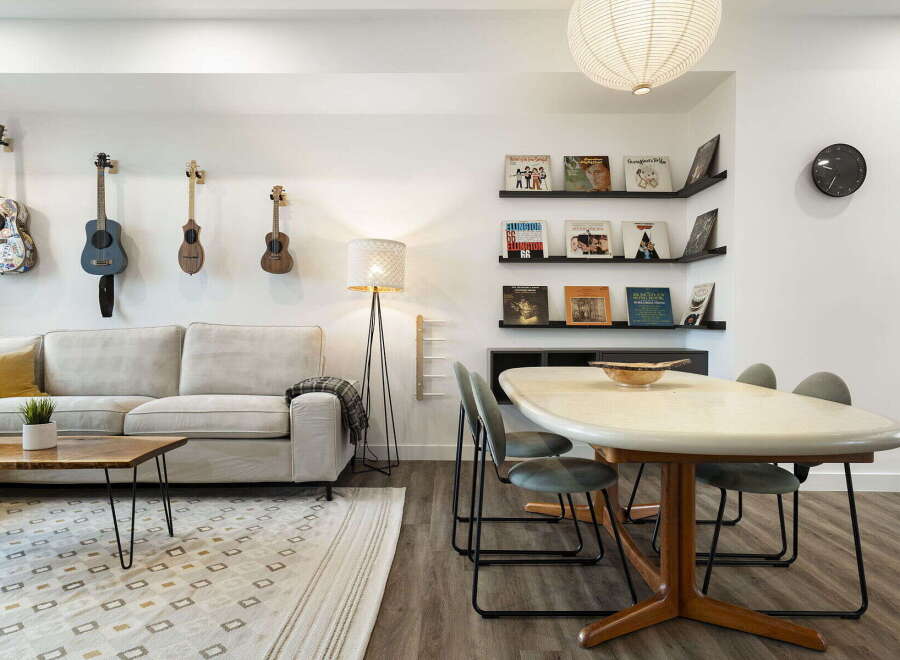 This stylish living and dining area features a comfortable cream sofa adorned with a plaid throw, complemented by a live-edge coffee table and a geometric rug.
