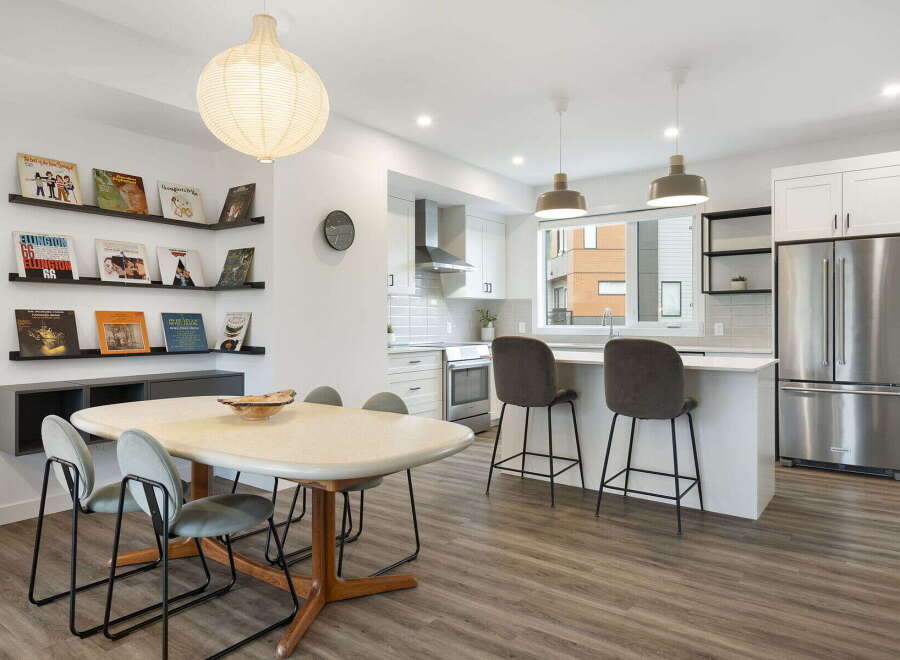 This modern open-concept living space features a stylish dining area with a unique table and chairs, adjacent to a sleek kitchen with stainless steel appliances and a breakfast bar.