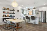 This modern open-concept living space features a stylish dining area with a unique table and chairs, adjacent to a sleek kitchen with stainless steel appliances and a breakfast bar.