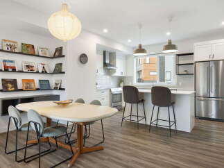 This modern open-concept living space features a stylish dining area with a unique table and chairs, adjacent to a sleek kitchen with stainless steel appliances and a breakfast bar.