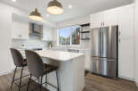Experience modern living in this stunning kitchen, featuring sleek white cabinetry, a spacious island with bar seating, and a large window offering picturesque views.