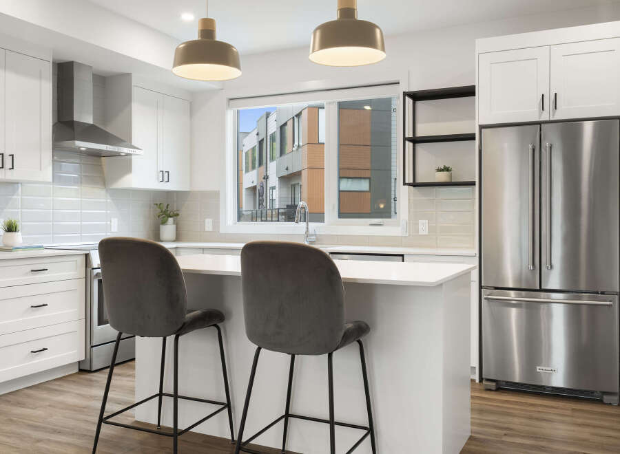 Experience modern living in this stunning kitchen, featuring sleek white cabinetry, a stainless steel range hood, and a spacious island perfect for casual dining.