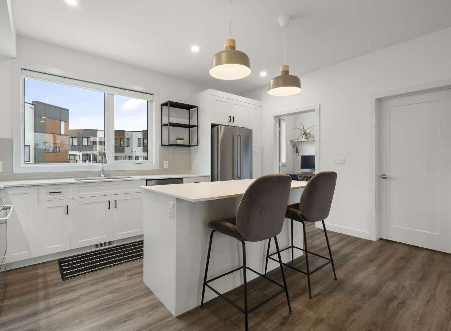 Experience modern living in this stunning kitchen featuring sleek white cabinetry, a spacious island with bar seating, and elegant pendant lighting.