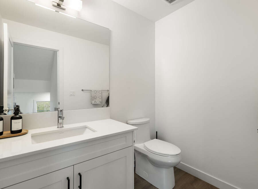 This modern bathroom features a sleek white vanity with a undermount sink and a chrome faucet, complemented by a large frameless mirror.