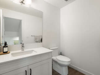 This modern bathroom features a sleek white vanity with a undermount sink and a chrome faucet, complemented by a large frameless mirror.