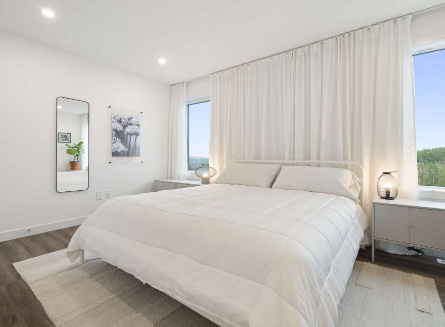 Experience serene comfort in this bright and airy bedroom, featuring a plush white duvet and a minimalist white metal bed frame.
