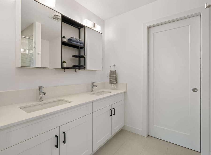 This modern bathroom features a spacious double vanity with sleek white countertops and undermount sinks, complemented by chrome faucets.