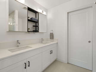 This modern bathroom features a spacious double vanity with sleek white countertops and undermount sinks, complemented by chrome faucets.
