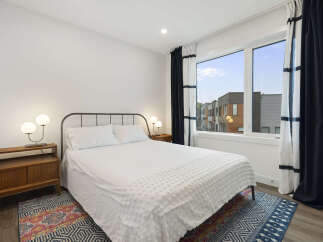 Experience modern comfort in this stylish bedroom, featuring a queen-sized bed with crisp white linens and a textured duvet.
