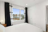 Experience modern living in this bright bedroom featuring a large window with scenic views of contemporary townhouses.