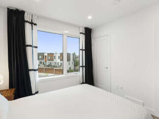 Experience modern living in this bright bedroom featuring a large window with scenic views of contemporary townhouses.