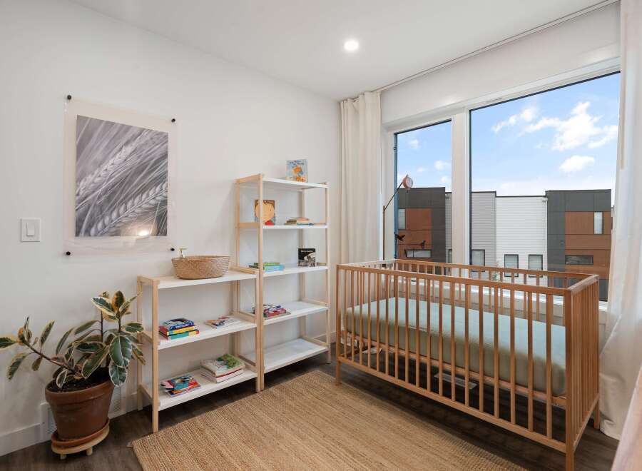 This charming nursery features a light wood crib positioned next to a large window with a view of modern townhouses.