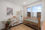 This charming nursery features a light wood crib positioned next to a large window with a view of modern townhouses.