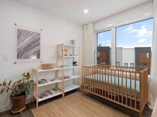 This charming nursery features a light wood crib positioned next to a large window with a view of modern townhouses.